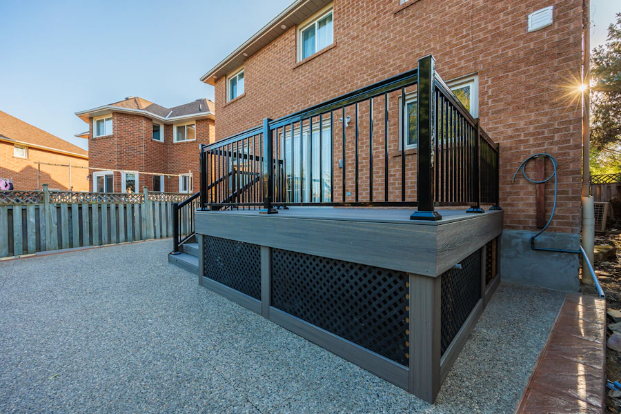 Raised composite deck with black aluminum railing and lattice skirting beside a brick house