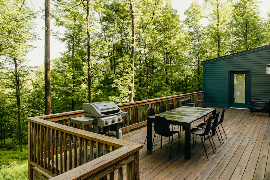 Wooden backyard deck with an outdoor dining table and barbecue among mature trees